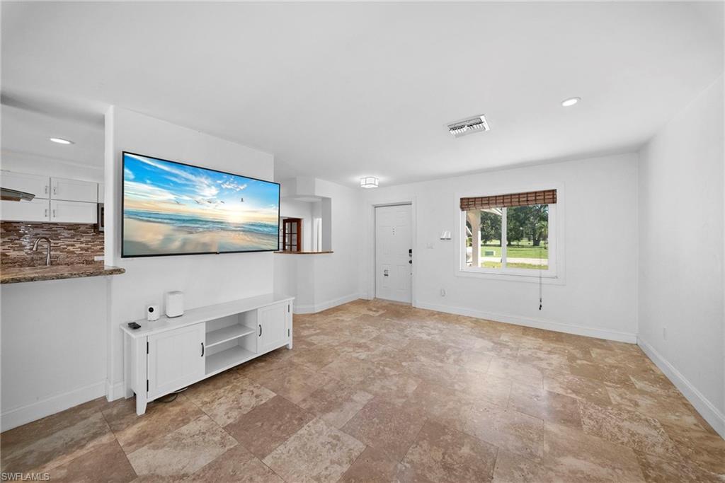 Open concept living area featuring large format tile flooring, a kitchen pass-through with granite countertop, recessed lighting, and a front window with a woven wood blind