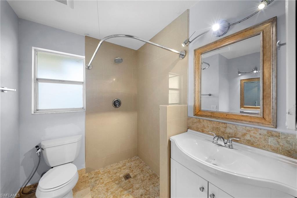 Bathroom featuring a tiled standing shower, white toilet, vanity with integrated sink, and a framed mirror with track lighting