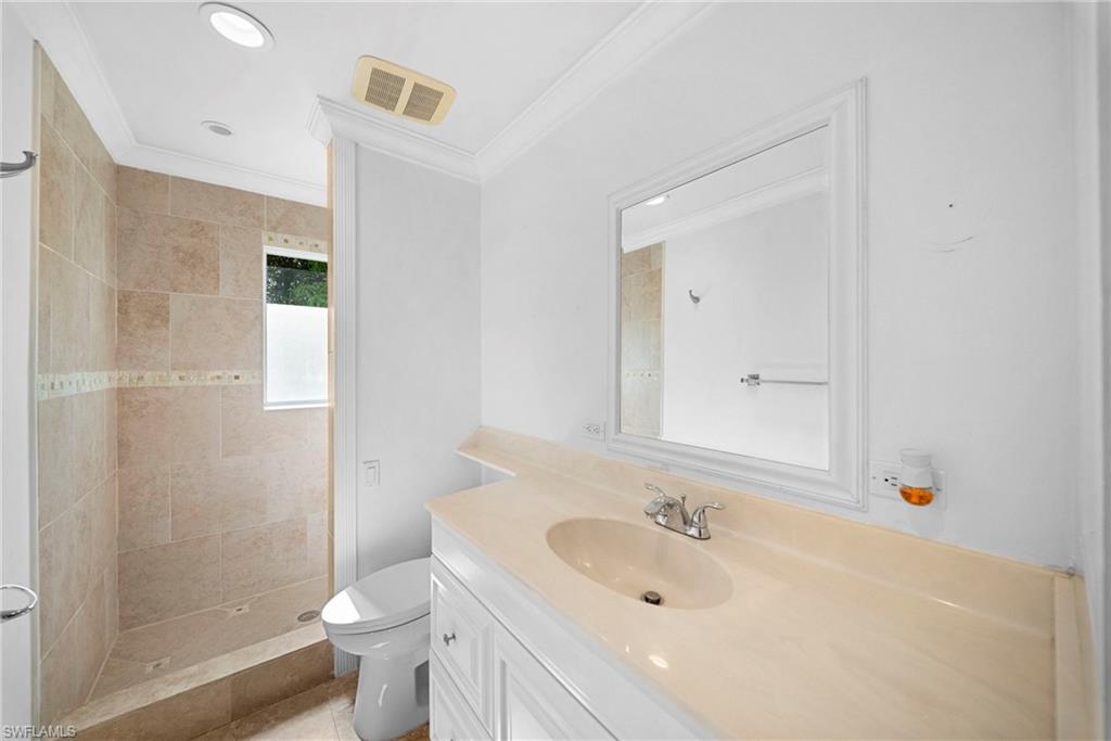 Bathroom featuring a walk-in shower with natural stone-look tile, a single vanity with a solid surface countertop, a recessed sink, and a framed mirror
