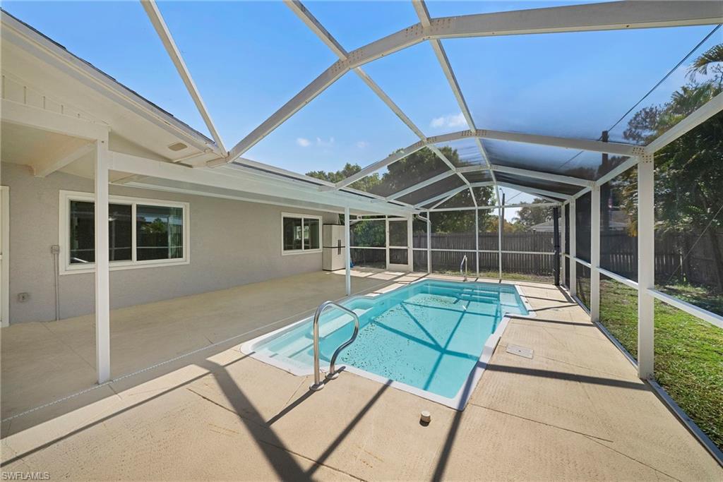 Screen-enclosed pool area featuring a rectangular swimming pool with integrated steps, a surrounding concrete deck, and a fenced perimeter