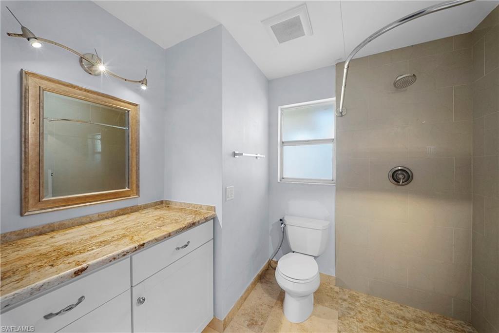 Bathroom featuring a vanity with a stone countertop, white cabinetry, and a framed mirror