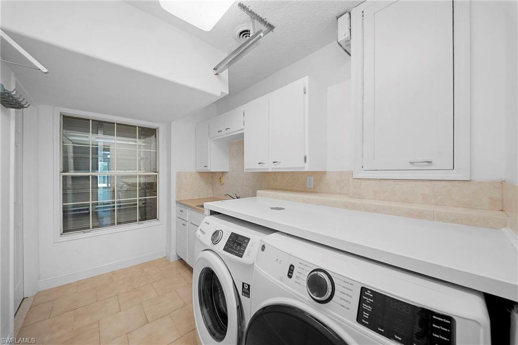 Dedicated laundry area featuring a front-load washer and dryer, extensive countertop space, a utility sink, white cabinetry, and tiled flooring