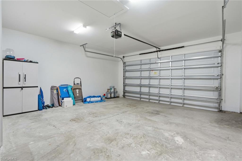 Spacious garage featuring a concrete floor, white walls, overhead lighting, and an automatic garage door opener