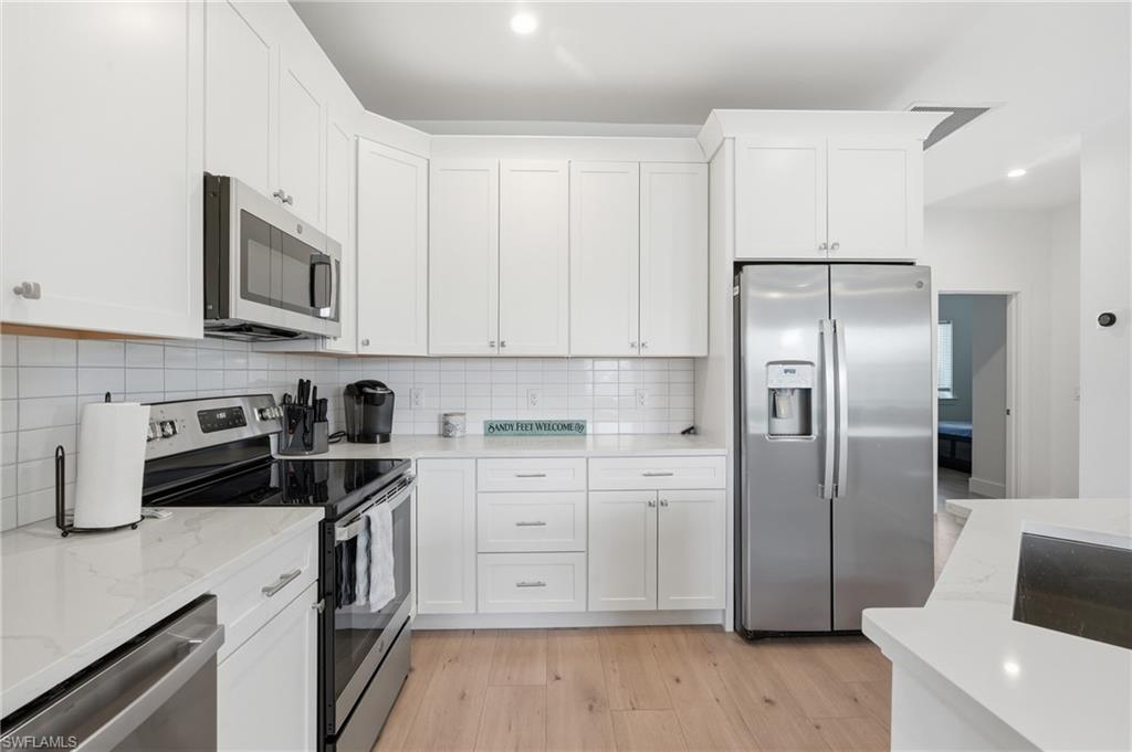 Kitchen featuring white shaker cabinetry, stainless steel appliances, light wood-finish flooring, white subway tile backsplash, and light-toned countertops