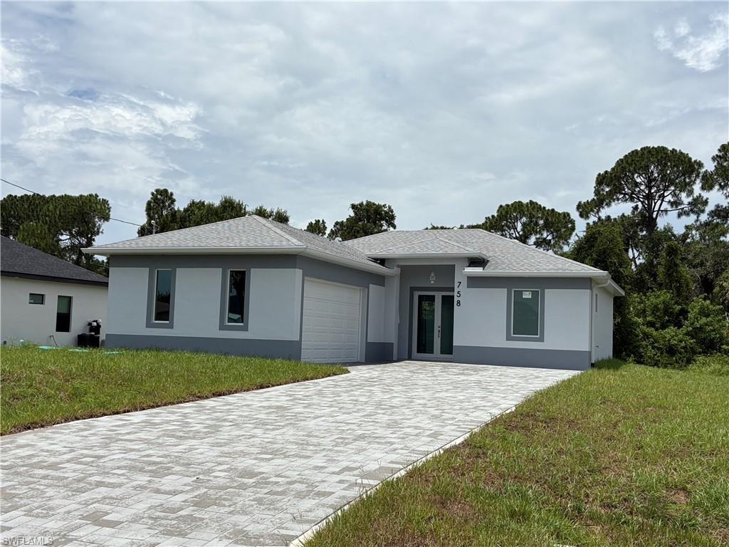 Modern one-story residence featuring a two-tone exterior, an attached garage, a paved driveway, a gabled roof, and a double-door entryway