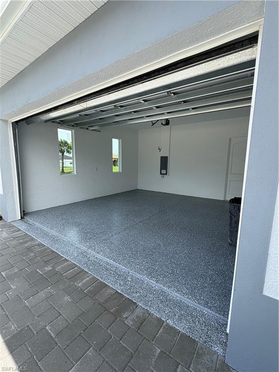 Spacious garage featuring a durable epoxy floor, white walls, two rectangular windows, and a paver driveway approach