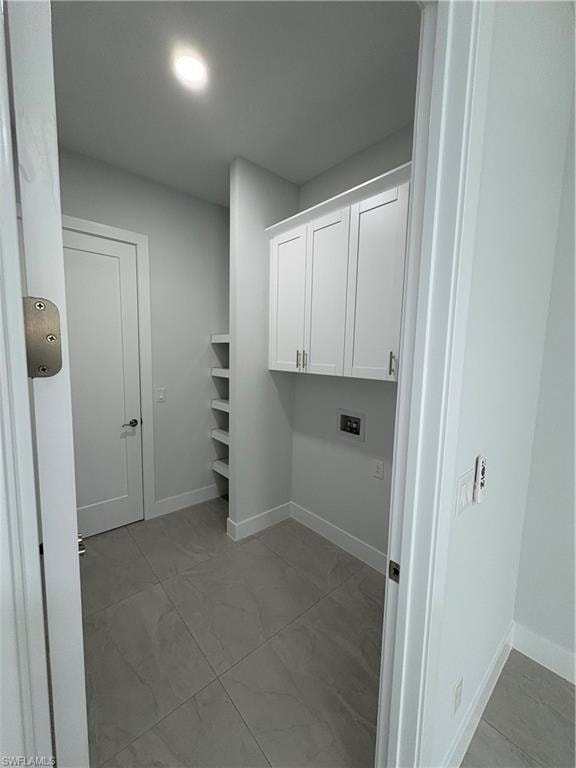 Utility room featuring light gray tile flooring, built-in shelving, white cabinetry with silver hardware, recessed lighting, and a white interior door