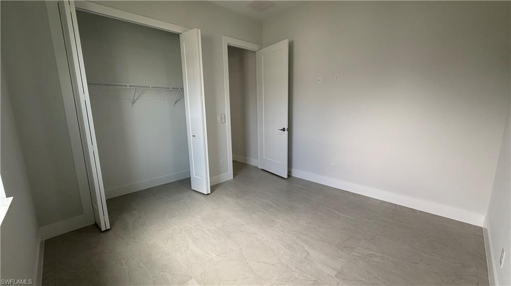 Room featuring light-toned large format tile flooring, a bi-fold closet with wire shelving, white baseboards, and a white interior door
