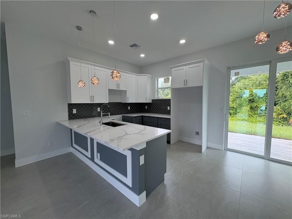 Contemporary kitchen featuring a large island with a waterfall countertop, white upper cabinetry, gray lower cabinetry, and a dark diamond-patterned backsplash