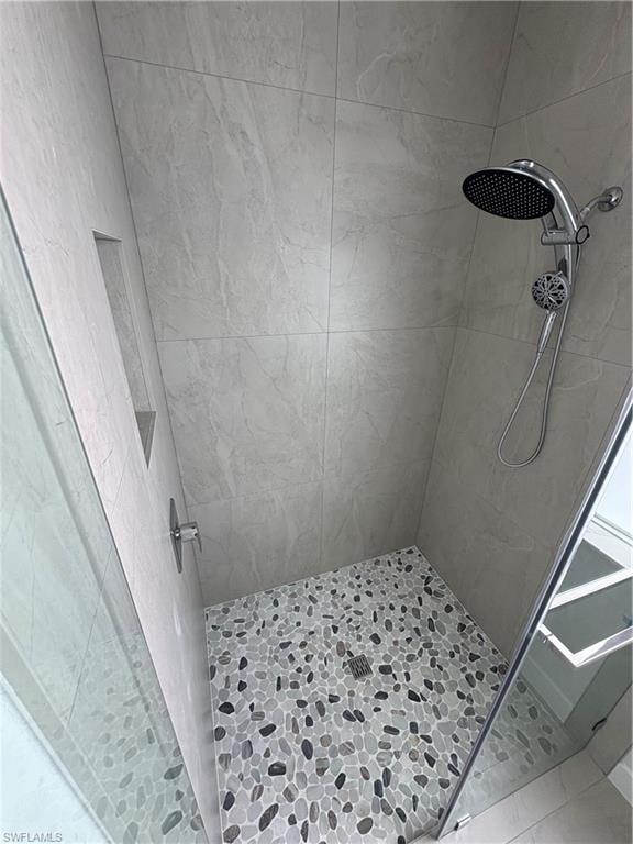 Spacious shower featuring light-toned tile walls and a pebble-tiled floor