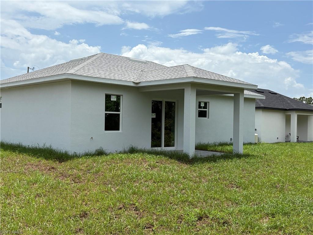 Rear exterior featuring a covered patio with white columns, light stucco finish, and a gray shingle roof