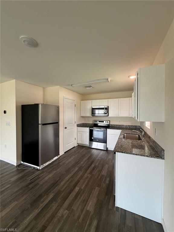 Modern kitchen featuring wood-finish flooring, white cabinetry, granite-style countertops, stainless steel appliances, and a double-basin sink