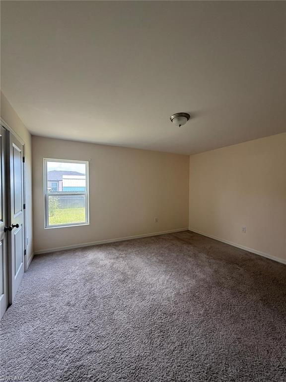 Spacious room featuring neutral-toned walls, gray carpeting, a single window, and a flush-mount ceiling light fixture