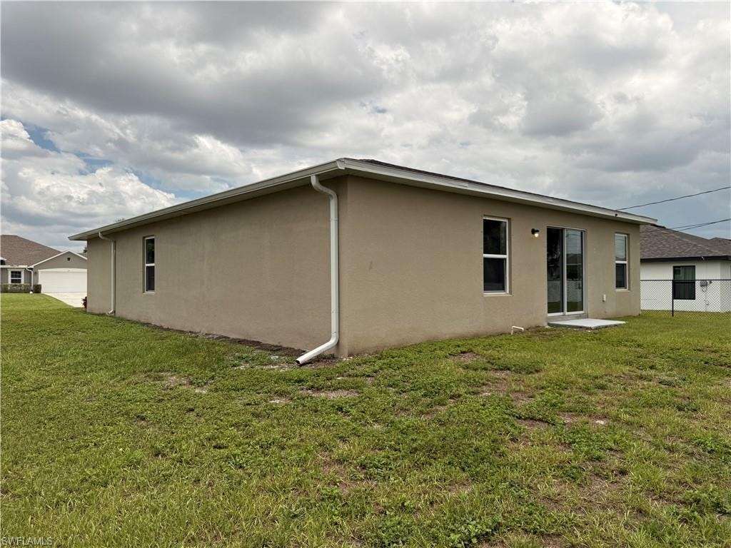 Stucco exterior with white trim, multiple windows, and sliding glass doors leading to a concrete pad