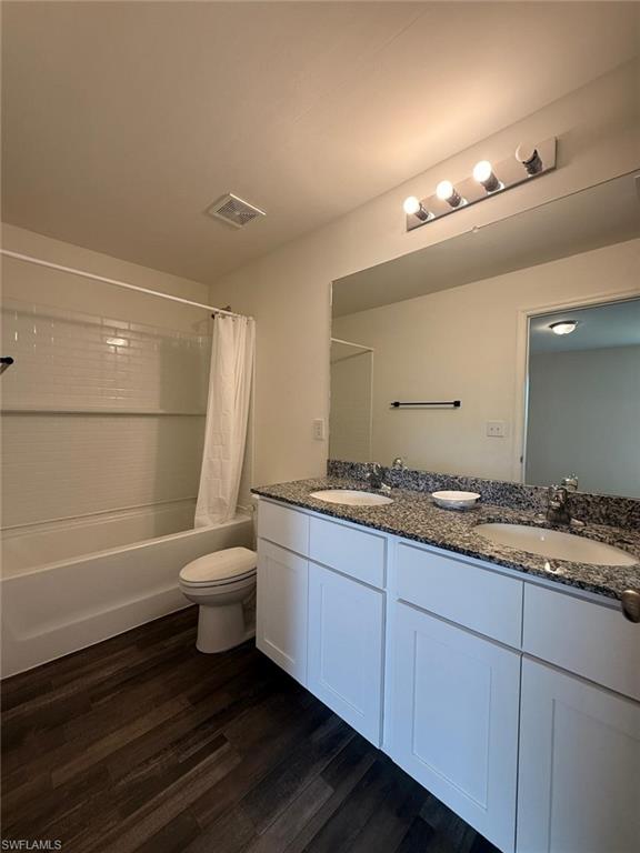 Bathroom featuring a dual vanity with a patterned countertop, white cabinetry, and wood-finish flooring