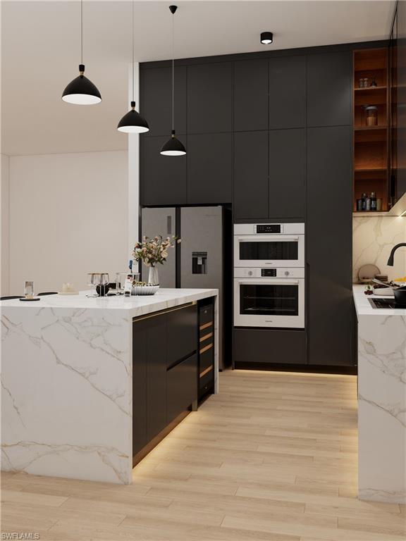 Kitchen featuring a waterfall island with stone-finish countertops, integrated wine cooler, light wood-finish flooring, and black cabinetry with built-in stainless steel appliances (Rendered photo)