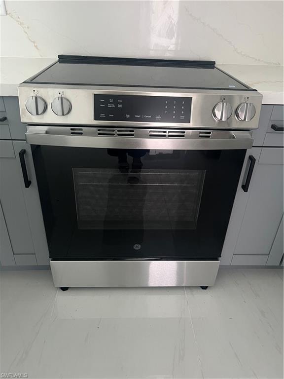 Stainless steel range with a glass cooktop and digital controls, integrated into a countertop featuring a subtle veining pattern