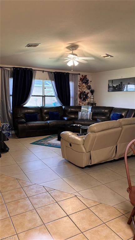 Spacious living area featuring light-toned square tile flooring, a ceiling fan with integrated lighting, and multiple windows