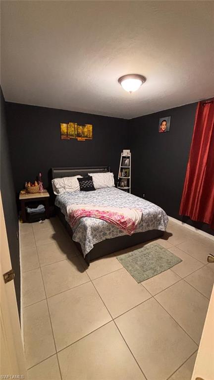 Bedroom featuring light-colored tile flooring, dark accent walls, and a ceiling-mounted light fixture