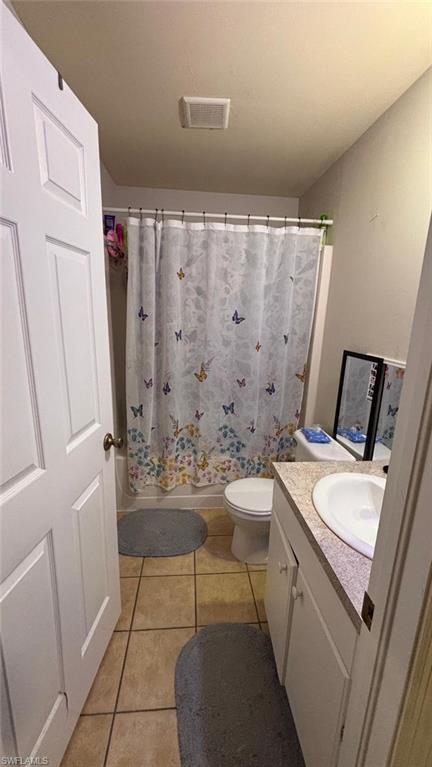 Bathroom featuring a single vanity with a white countertop and integrated sink, a built-in tub with shower, and ceramic tile flooring