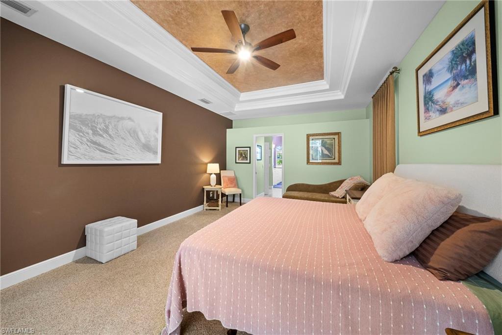 Tray ceiling with crown molding, ceiling fan, and carpet flooring