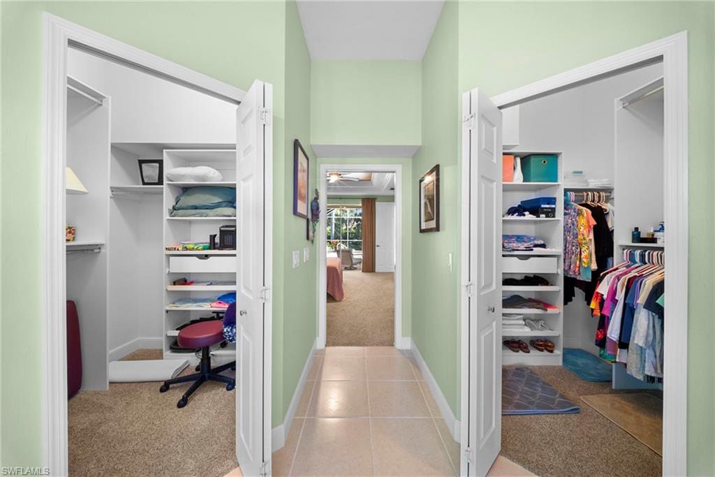 Hallway with tile flooring, dual closets featuring built-in shelving, and carpeted closet interiors