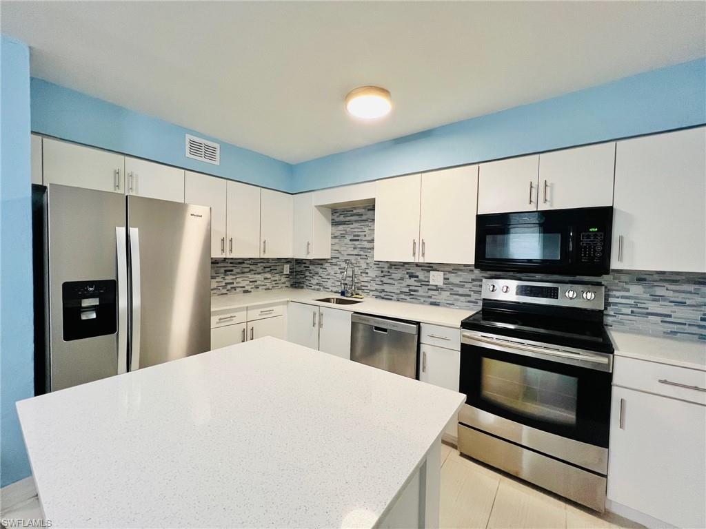 Kitchen featuring an island with a light-colored countertop, white cabinetry, stainless steel appliances, and a mosaic tile backsplash