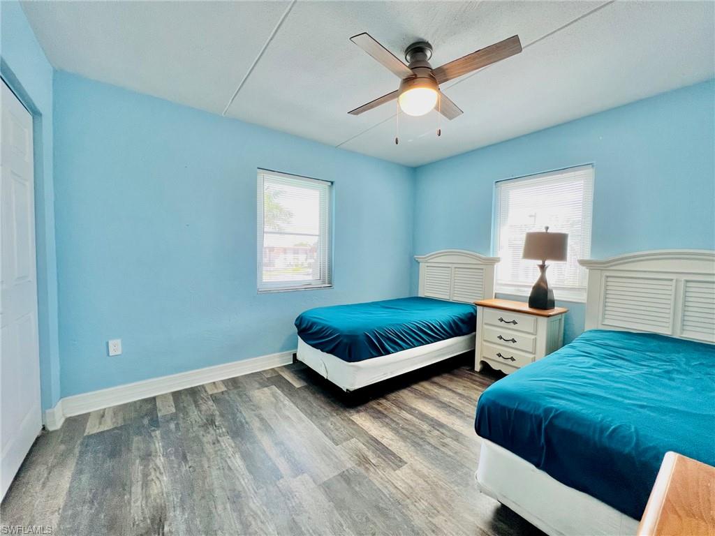 Room featuring wood-finish flooring, two windows with white blinds, and a ceiling fan with integrated lighting
