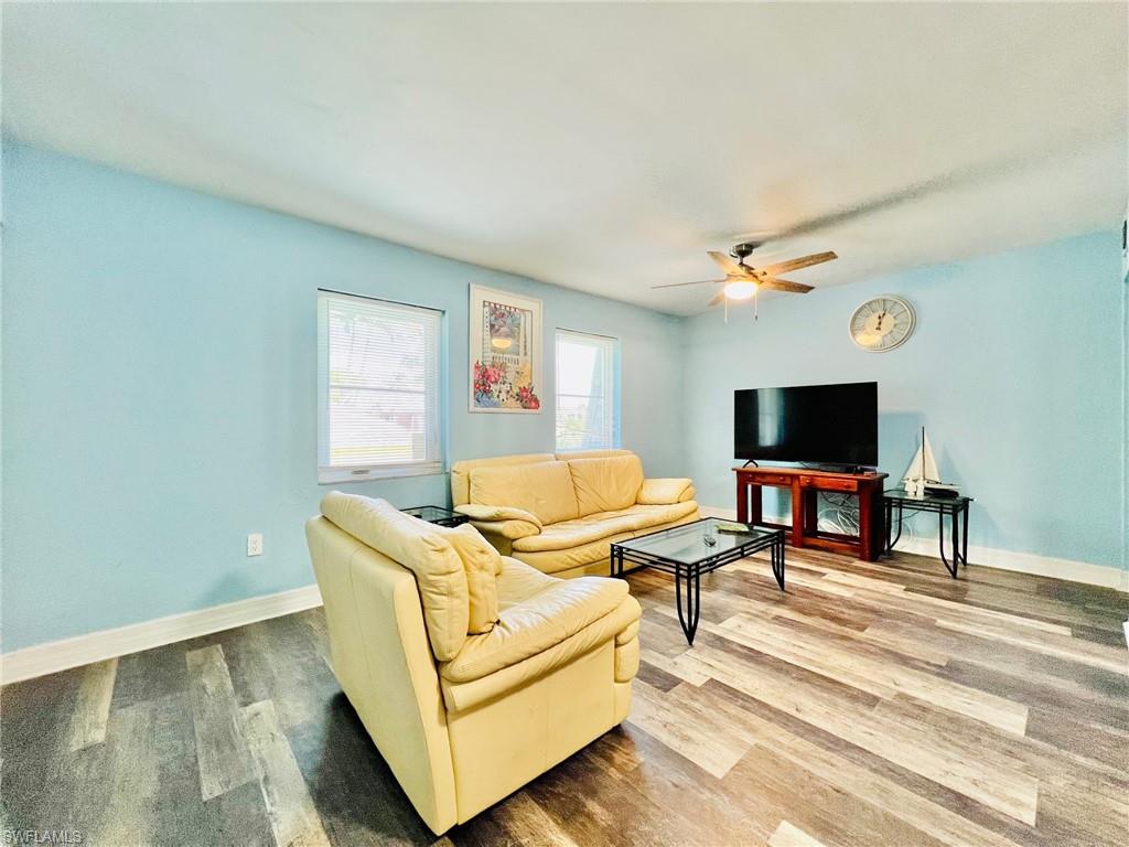 Living area featuring wood-finish flooring, two windows providing natural light, a ceiling fan, and light blue wall tones
