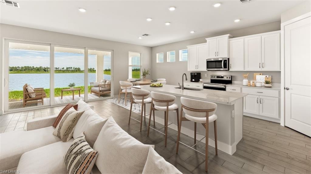 Sliding glass doors opening to a large patio, modern kitchen with white cabinetry, stainless steel appliances, a center island with bar seating, and wood-finish flooring