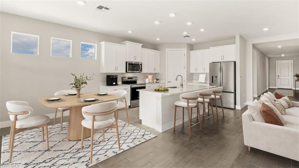 Open-concept living area with wood-finish flooring, recessed lighting, and a kitchen featuring white cabinetry, stainless steel appliances, and a central island with bar seating