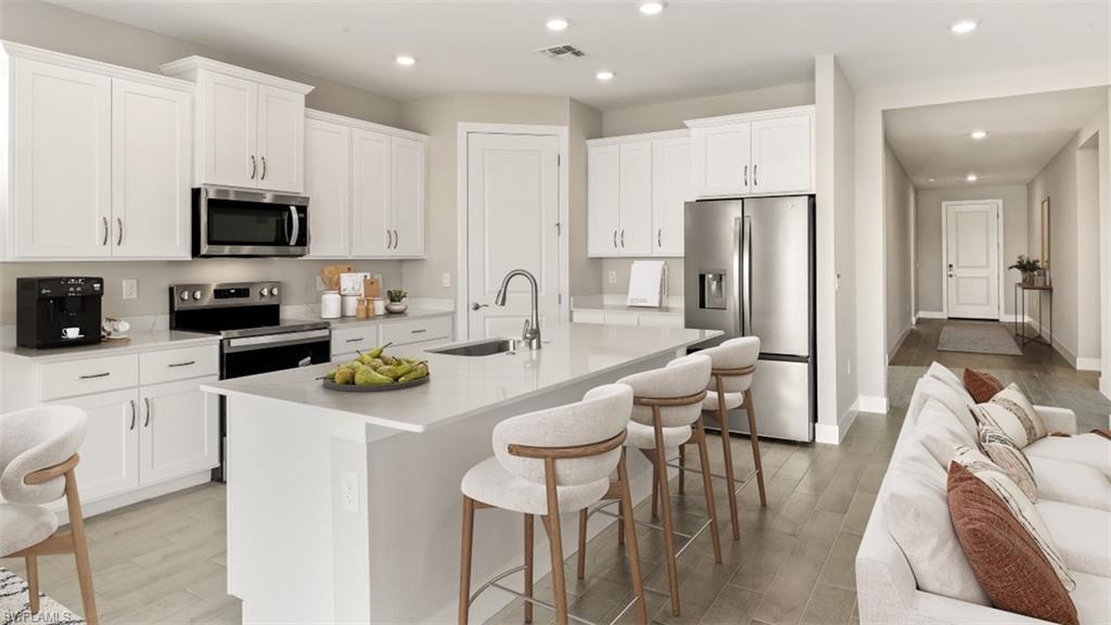 Kitchen featuring white shaker cabinetry, stainless steel appliances, a center island with countertop seating, and wood-finish flooring