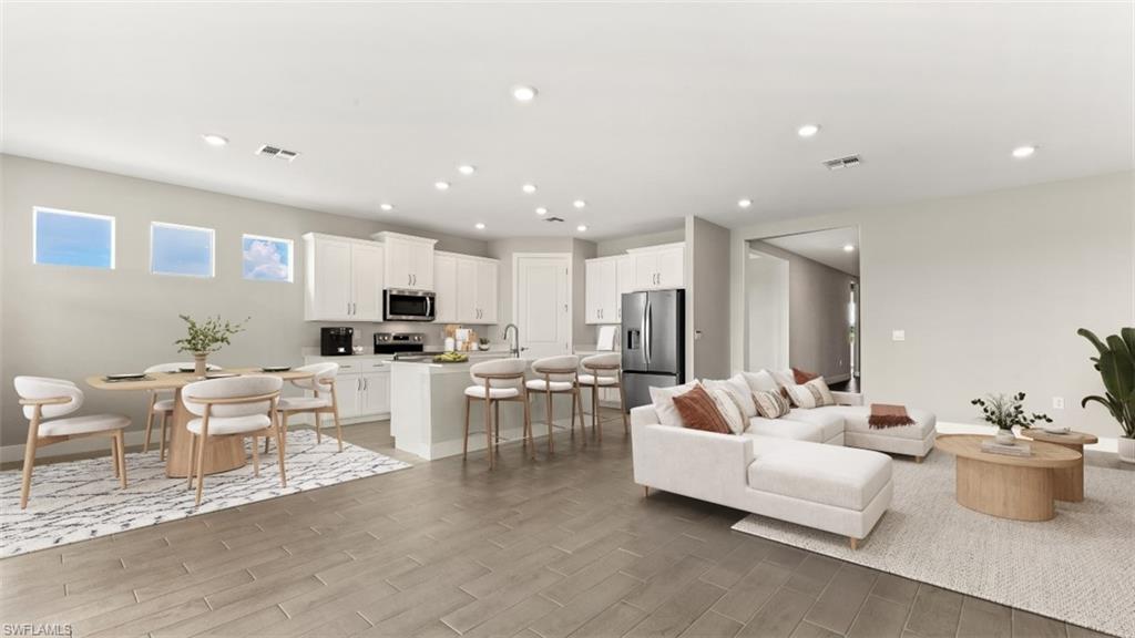 Recessed lighting throughout, wood-finish flooring, white cabinetry, and stainless steel appliances