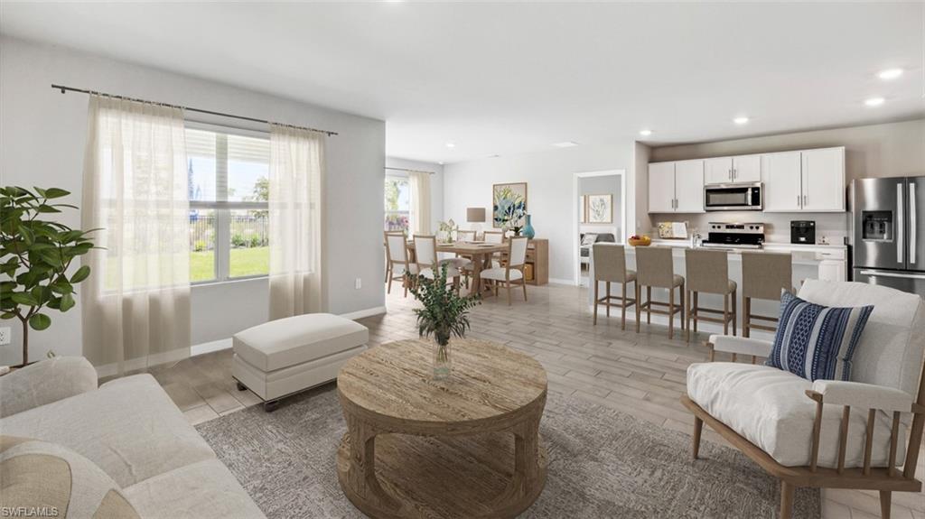 Open-concept living area featuring wood-finish flooring, a kitchen island with seating, white cabinetry, stainless steel appliances, and abundant natural light