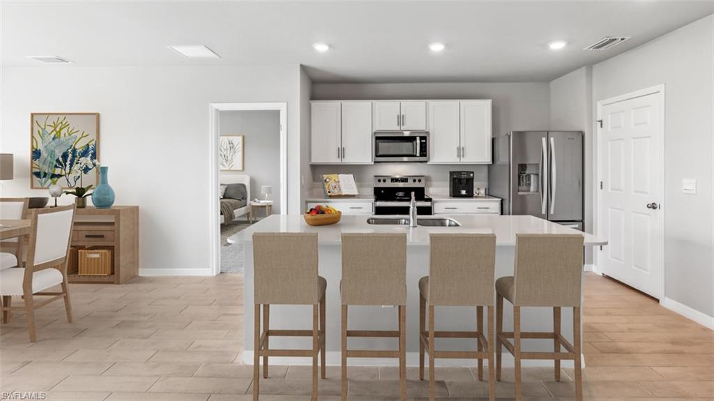 Modern kitchen featuring an island with seating, stainless steel appliances, white cabinetry, and recessed lighting