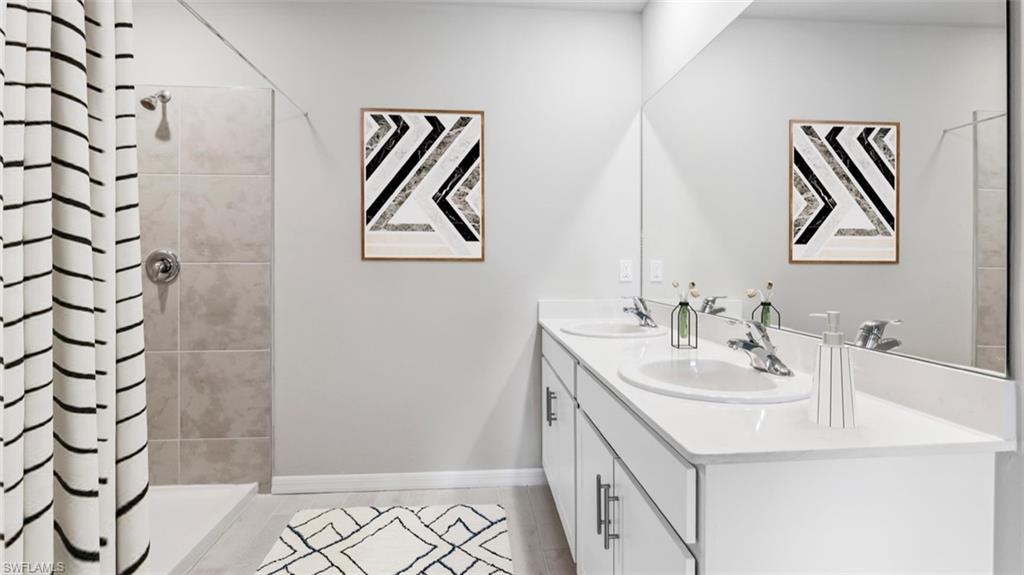 Bathroom featuring a dual vanity with undermount sinks and chrome fixtures, a full-width mirror, a shower with neutral-toned tiled walls, and light-toned flooring