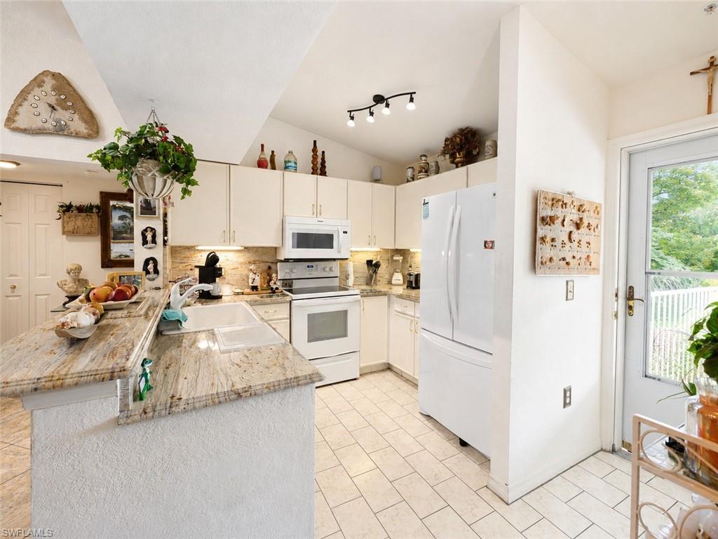 Kitchen featuring granite countertops, white cabinetry, tile flooring, and vaulted ceilings with track lighting