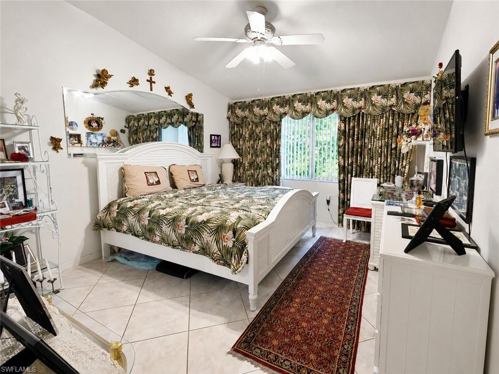 Vaulted ceiling bedroom featuring a ceiling fan, tiled flooring, and a large window with vertical blinds