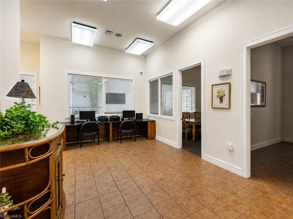 Spacious common area featuring durable tile flooring, multiple workstations with built-in desks, ample natural light from exterior windows, and bright overhead lighting