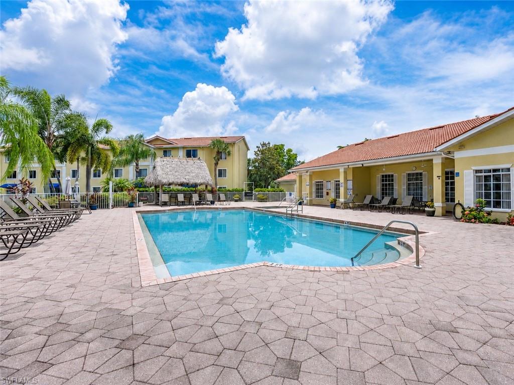 Outdoor swimming pool surrounded by paver decking, a thatched-roof cabana, and tropical landscaping