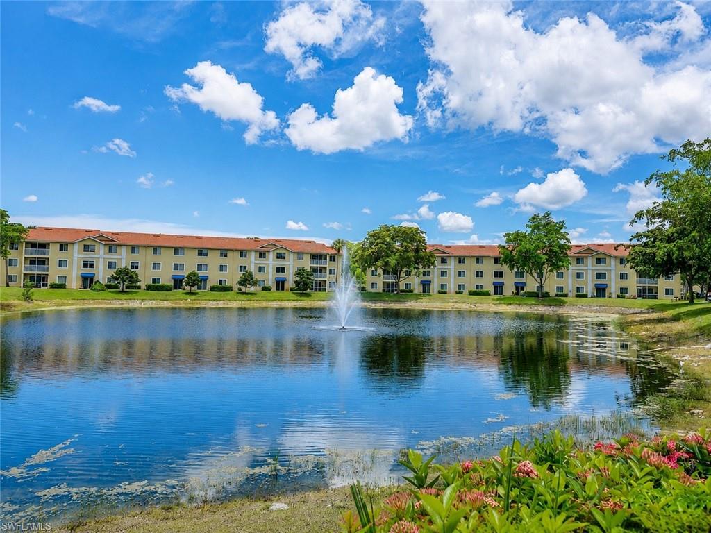 Waterfront condominium building featuring a central fountain, lush green landscaping, and mature trees