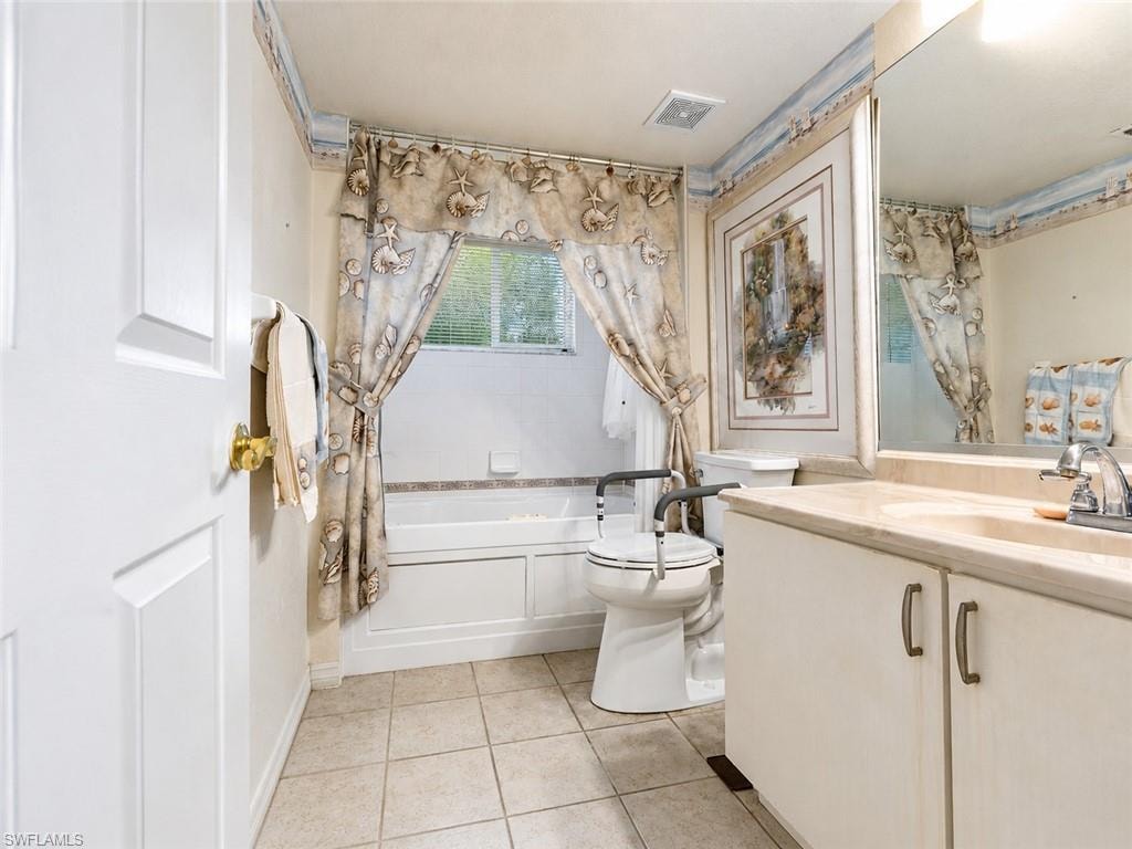 Bathroom featuring a built-in bathtub, a window, a single vanity with a solid surface countertop, and ceramic tile flooring