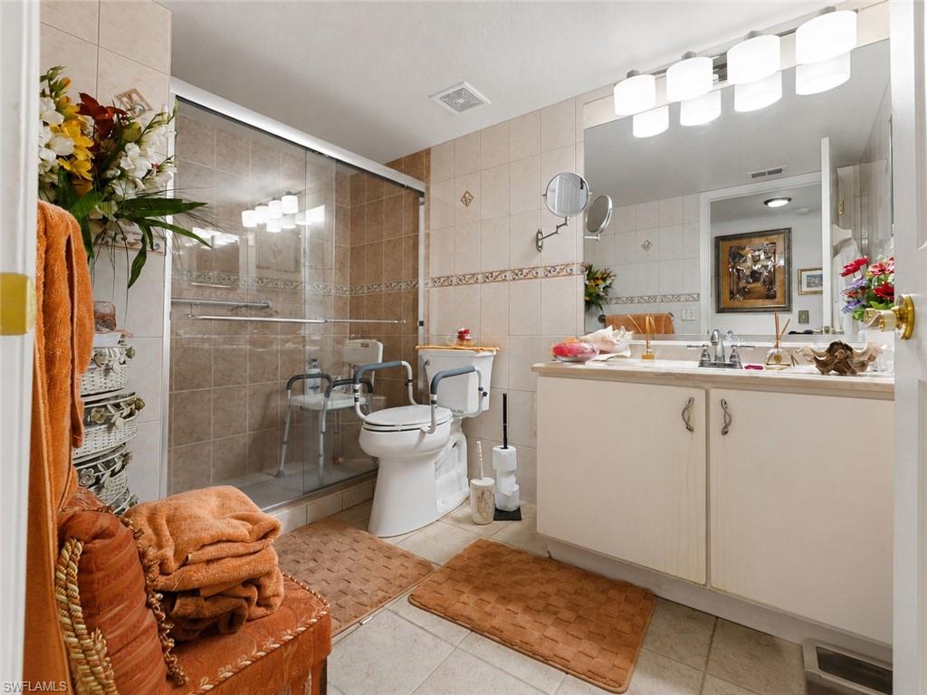 Bathroom featuring a shower with glass enclosure, ceramic tile walls, and a single vanity with storage cabinetry and a large mirror
