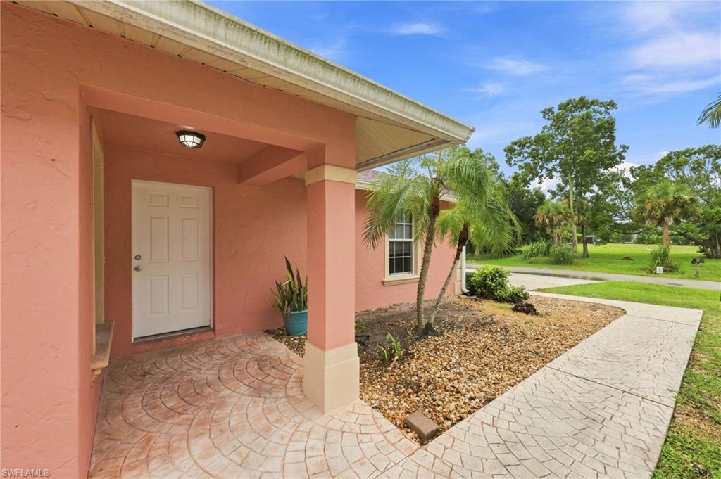 Welcoming covered entry featuring a coral stucco exterior, white paneled entry door, and decorative wall-mounted lighting