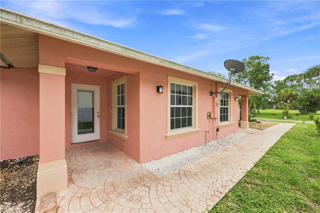 Coral stucco exterior with a covered front porch featuring a curved brick paver entry and multiple large windows with dark frames