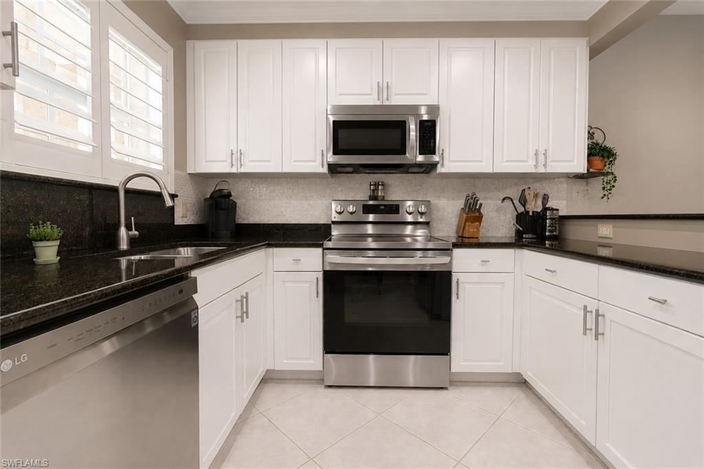 Kitchen featuring white cabinetry, dark stone countertops, stainless steel appliances, and a tile backsplash