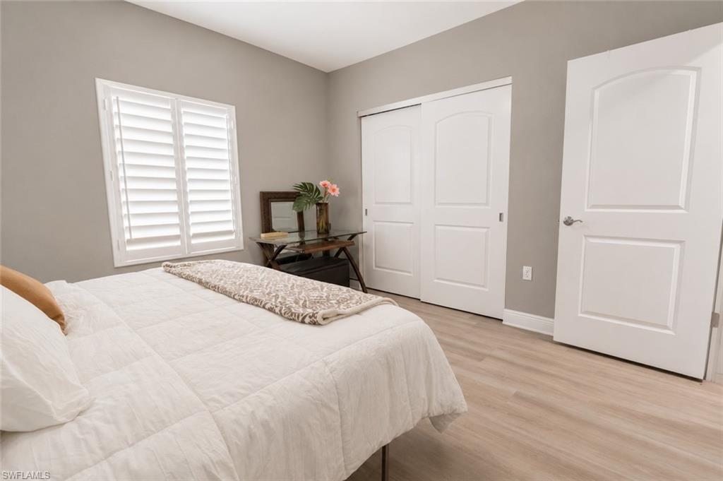 Bedroom featuring wood-finish flooring, a window with white plantation shutters, and a sliding closet door system
