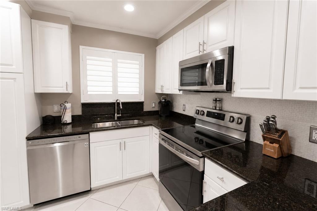 Kitchen featuring white shaker-style cabinetry, dark speckled countertops, and stainless steel appliances including a built-in microwave, range, and dishwasher