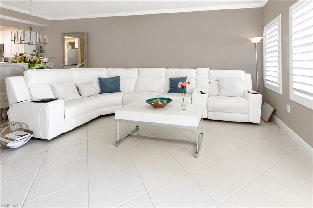Living area featuring large format tile flooring, a neutral wall color, crown molding, and plantation shutters