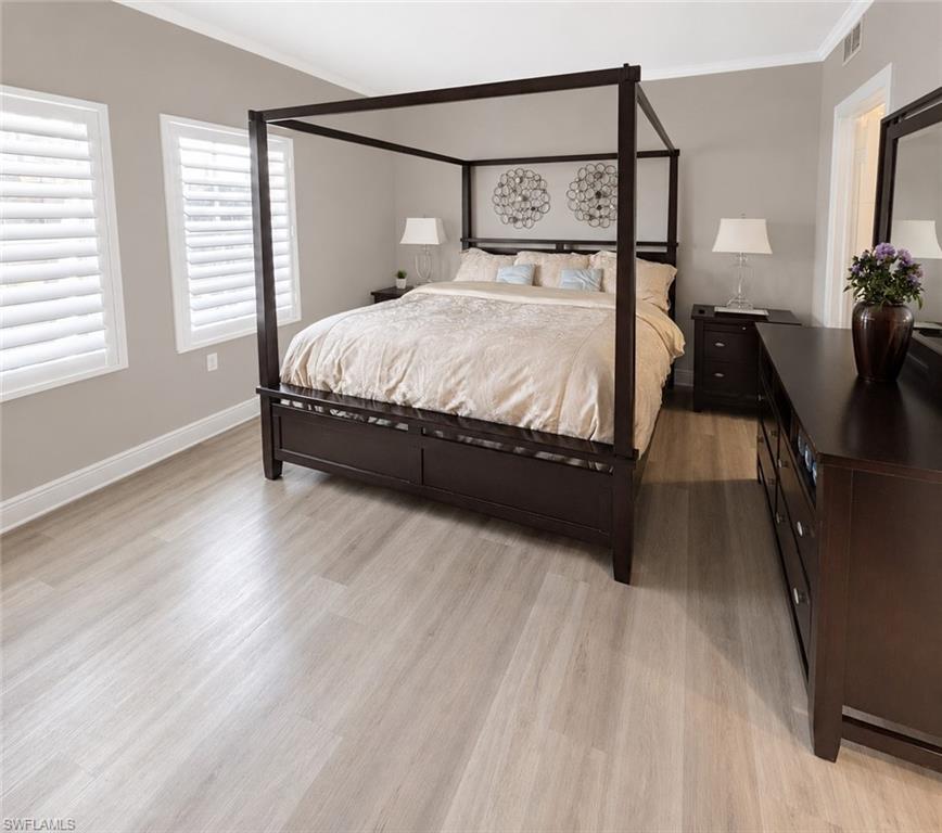 Spacious room featuring light wood-finish flooring, plantation shutters on two windows, crown molding, and a solid door frame